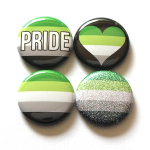 May include: Four round green, white, and gray pride buttons. One button says "PRIDE" in white letters. One button has a green, white, and gray heart. One button has a green, white, and gray stripe pattern. One button has a green, white, and gray stripe pattern with glitter.