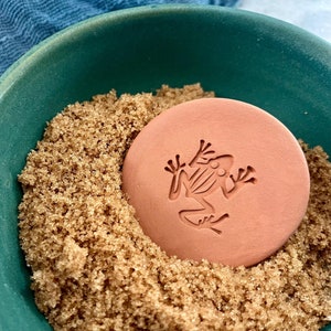 May include: A terracotta frog-shaped humidity control disc in a green bowl filled with brown sugar.