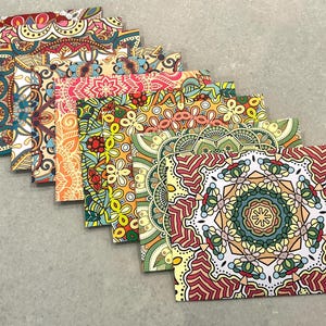 May include: A set of eight square greeting cards arranged in a cascading diagonal line. Each card features a unique, intricate, symmetrical mandala pattern in vibrant colours including red, yellow, orange, green, blue, and white, with detailed geometric shapes.