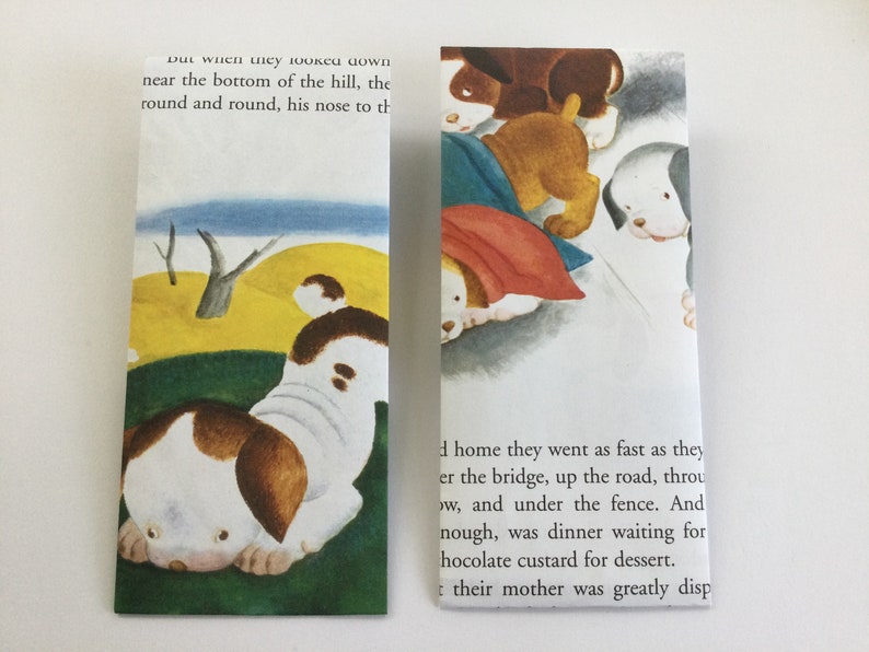 May include: Two bookmarks with illustrations of puppies from a children's book. One bookmark shows a puppy with brown and white markings, while the other shows several puppies. Text from the book is visible.