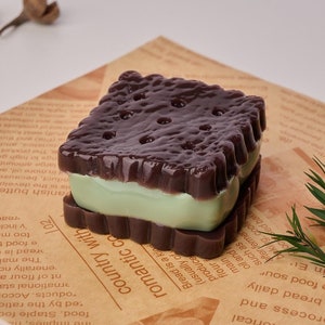 May include: A close-up of a chocolate and green layered dessert with a textured surface. The dessert is on a brown paper background.