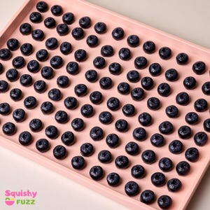 May include: A pink tray filled with approximately 100 small, dark blue, round, blueberry-shaped objects.