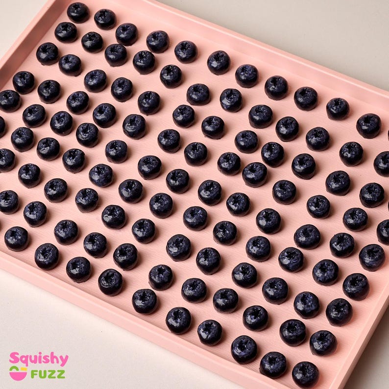 May include: A pink tray filled with approximately 100 small, dark blue, round, blueberry-shaped objects.