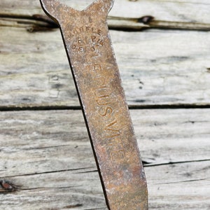 May include: A rusty metal wrench with a hexagonal opening and the words 'LUSVITE' and 'RIFLE' stamped on the handle.
