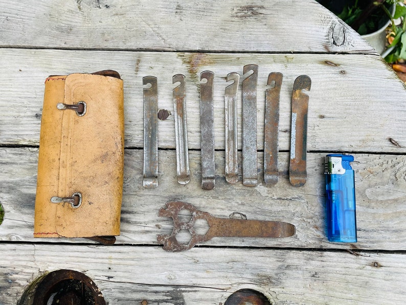 May include: A set of tire levers, a wrench, and a blue lighter on a wooden surface. The tire levers are made of metal and have a rusty finish. The wrench is also made of metal and has a rusty finish. The lighter is made of plastic and has a blue finish.