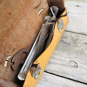 May include: A yellow leather tool roll with a red trim and flower-shaped metal accents. The roll is open and contains several rusty metal tools.
