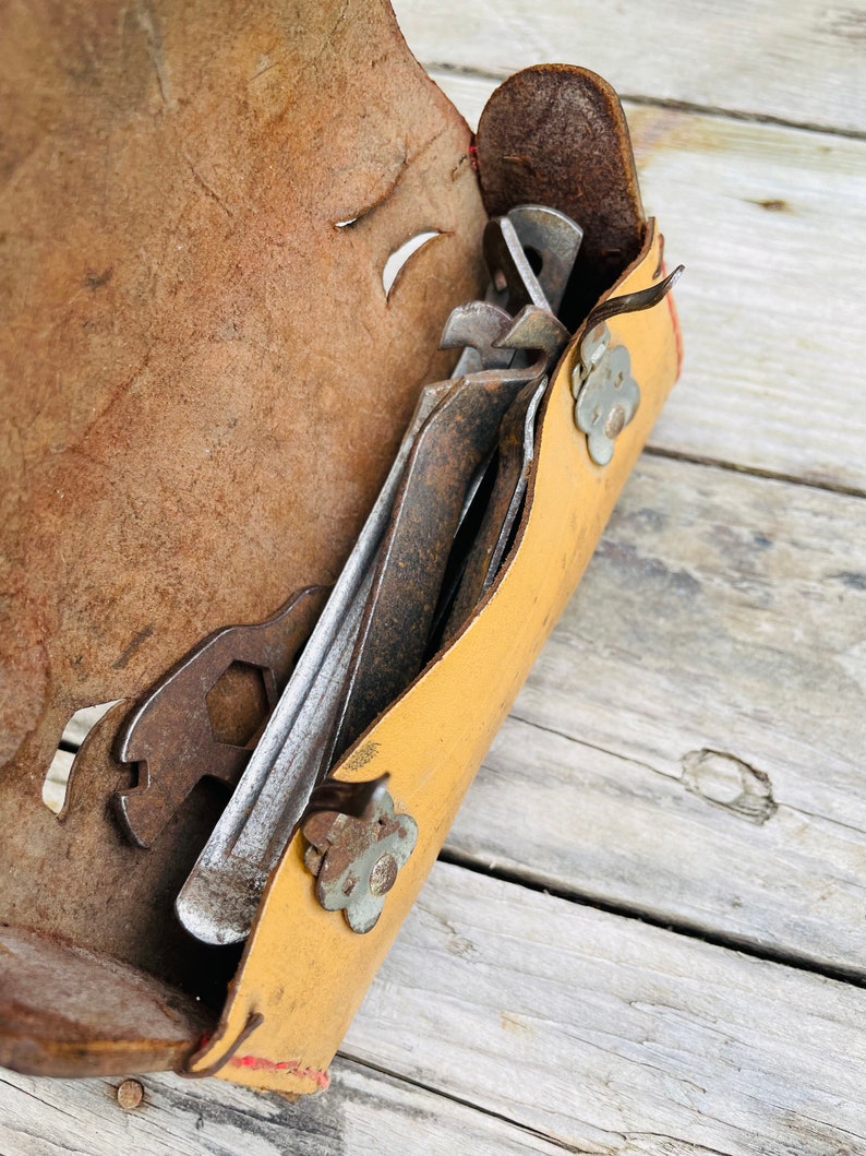 May include: A yellow leather tool roll with a red trim and flower-shaped metal accents. The roll is open and contains several rusty metal tools.