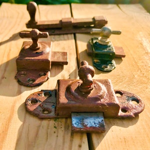 May include: Four antique metal door latches in various styles and colors. The latches are made of metal and have a rustic, aged look. They are all in different stages of wear and tear, with some showing signs of rust and others having a more polished finish.