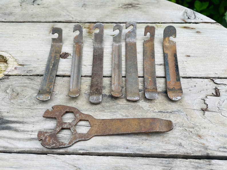 May include: Eight rusty metal tire levers and a rusty metal wrench with a hexagonal hole in the center. The wrench has the words 'THIS WAS MY' stamped on it.
