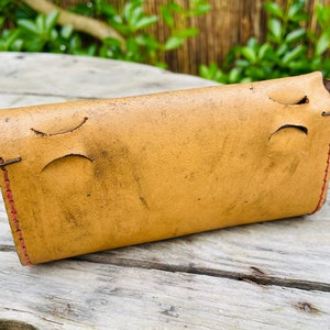 May include: A light brown leather wallet with red stitching. The wallet has two cutouts on the back side.