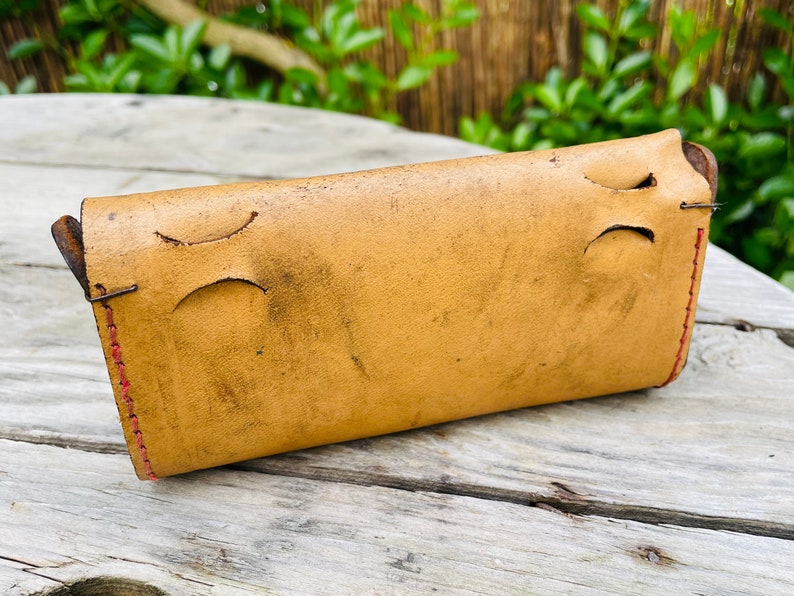 May include: A light brown leather wallet with red stitching. The wallet has two cutouts on the back side.