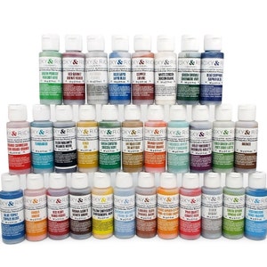 May include: A collection of 36 small bottles of paint arranged in a pyramid shape. The bottles are labeled with the names of different colors and minerals, such as "Green Peridot", "Red Garnet", "Blue Lapis", "Copper", "White Zircon", "Green Emerald", "Blue Sapphire", "Orange Carnelian", "Turquoise", "Black Malachite", "Gold", "Green Crystal", "Antique Gold", "Orange Garnet", "Apatite Turquoise", "Violet Rhodolite", "Sold Green Lustre", "Bronze", "Blue Topaz", "Amber", "Red Ruby", "Pink Quartz", "Silver", "Green Sphene", "Aigue-Marine", "Yellow Chrysoberyll", "Caramel Satin", "Orange Amber", "Shadow Blue", "Pearlescent Lavender", "Strained Ochre", "Cobalt Blue", "Pink Rose", "Argent", "Green Spinel", "Magma-Marine".