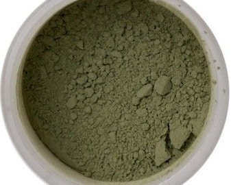 May include: A close-up view of a small, round container filled with a fine, light green powder. The powder is evenly distributed and appears to be a natural ingredient.