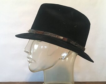 May include: A black fedora hat with a brown and black patterned band. The hat is on a clear plastic mannequin head.