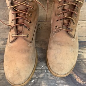 Puede incluir: Un par de botas de cuero marr&oacute;n con cordones amarillos. Las botas est&aacute;n gastadas y tienen un aspecto desgastado.