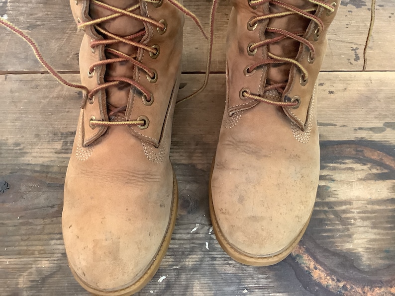 Puede incluir: Un par de botas de cuero marr&oacute;n con cordones amarillos. Las botas est&aacute;n gastadas y tienen un aspecto desgastado.