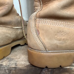 Puede incluir: Un par de botas de cuero color canela con costuras blancas y suela de goma marr&oacute;n. Las botas tienen un logotipo en el lateral que dice "Timberland" con un logotipo de &aacute;rbol.