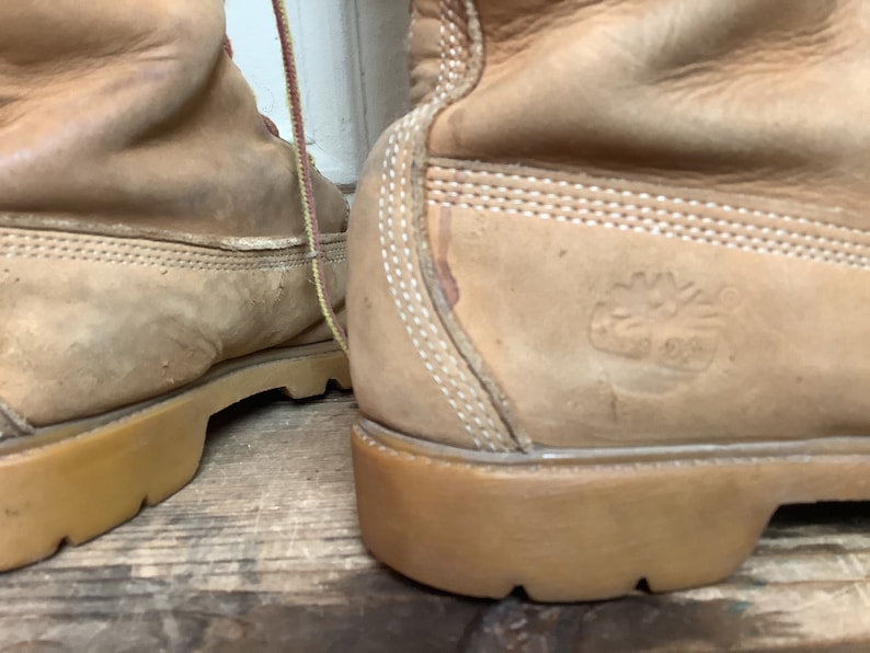 Puede incluir: Un par de botas de cuero color canela con costuras blancas y suela de goma marr&oacute;n. Las botas tienen un logotipo en el lateral que dice "Timberland" con un logotipo de &aacute;rbol.