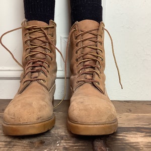 Puede incluir: Un par de botas de cuero marr&oacute;n con cordones amarillos. Las botas est&aacute;n atadas y tienen un aspecto desgastado.