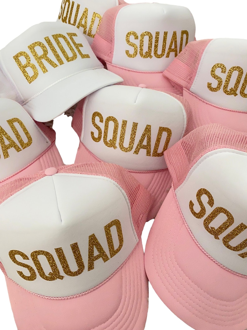 May include: Pink and white trucker hats with gold glitter lettering. The hats say "Bride" and "Squad".
