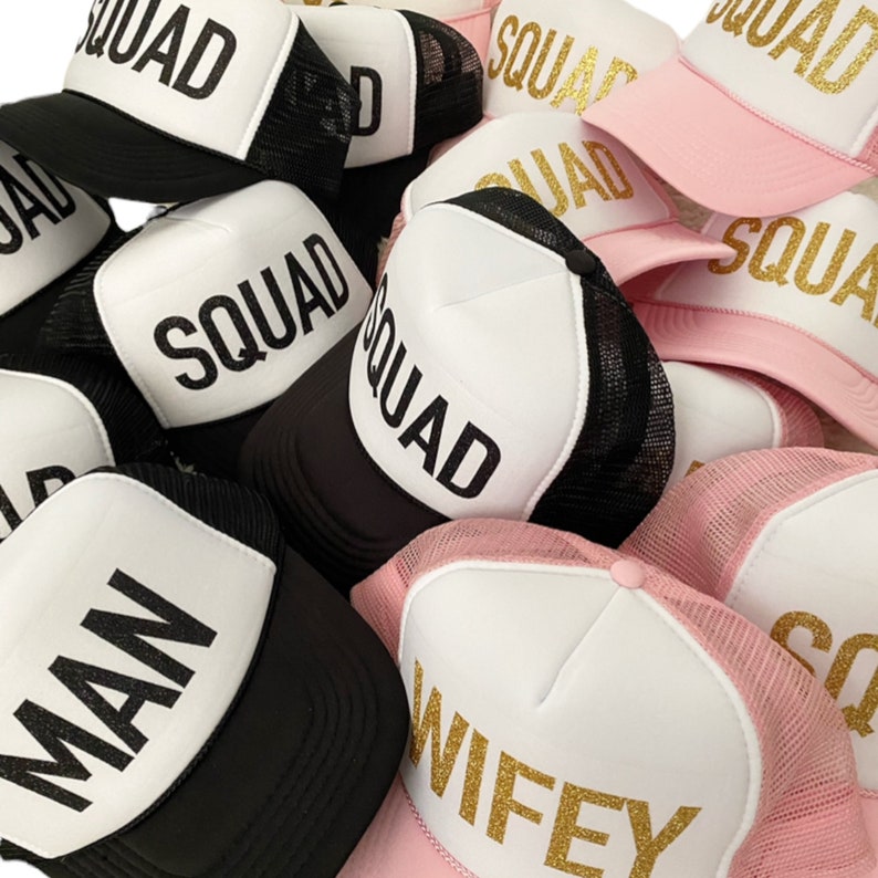 May include: A group of black and pink trucker hats with white mesh panels. The hats have gold glitter lettering that says "Squad", "Man", "Wifey", and "Squad" on them.