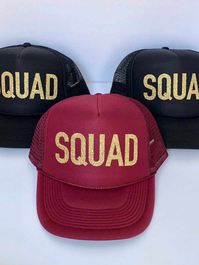 May include: Three trucker hats with the word "SQUAD" in gold glitter lettering. One hat is black, one is maroon, and one is black.