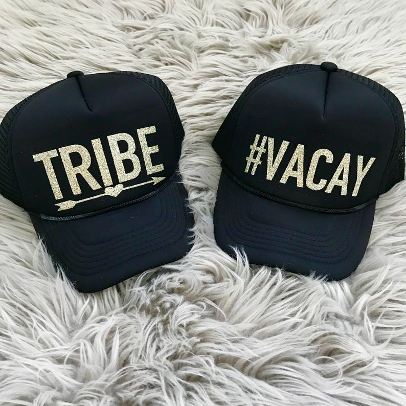 May include: Two black trucker hats with gold glitter lettering. One hat says "TRIBE" with an arrow and heart. The other hat says "#VACAY".