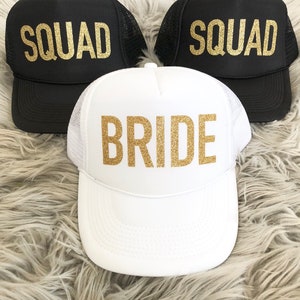 May include: Three trucker hats with gold glitter lettering. One white hat says "BRIDE" and two black hats say "SQUAD".
