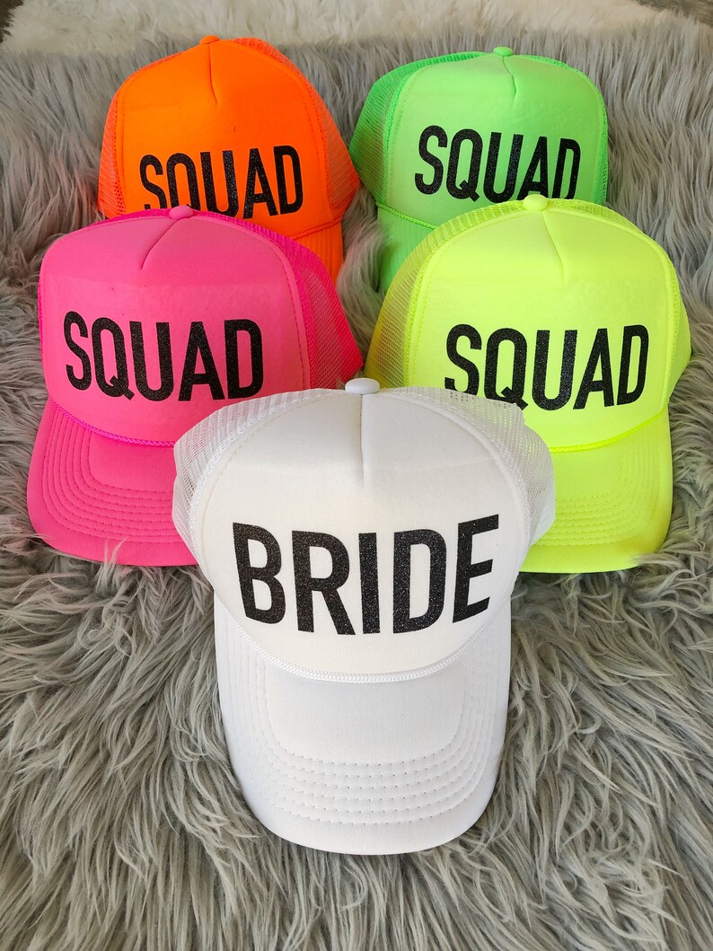 May include: Five neon coloured trucker hats with black mesh backs. Four hats say "SQUAD" in black lettering and one hat says "BRIDE" in black lettering.