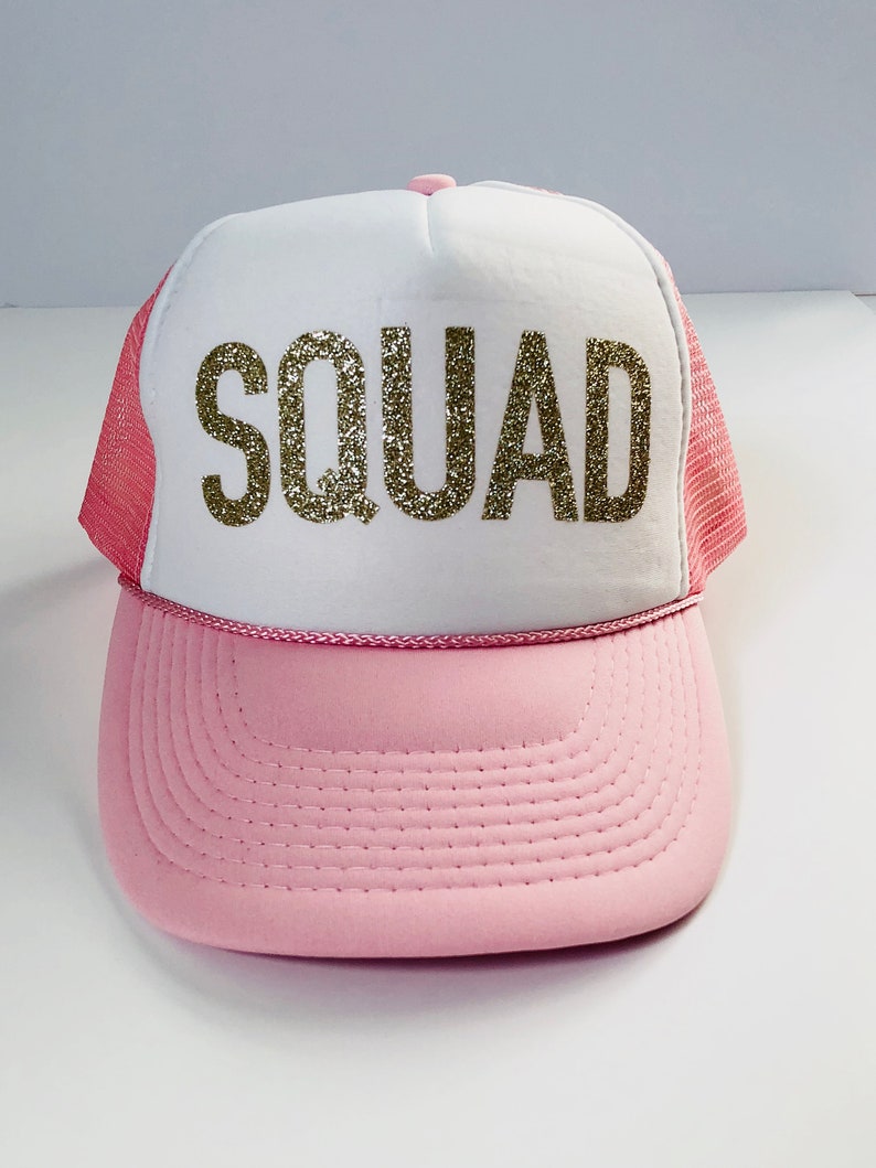 May include: A pink and white trucker hat with a gold glitter "SQUAD" design.