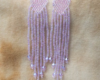 May include: A pair of long, beaded earrings with a light purple iridescent finish. The earrings are made of small, round beads and have a teardrop shape.