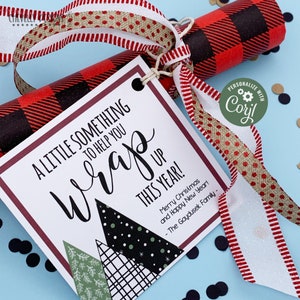 May include: A white card with red trim and a black and white geometric design. The card reads "A little something to help you wrap this year! Merry Christmas and Happy New Year! - The Gaydusek Family". The card is tied with a red and white ribbon and a gold ribbon with white polka dots.