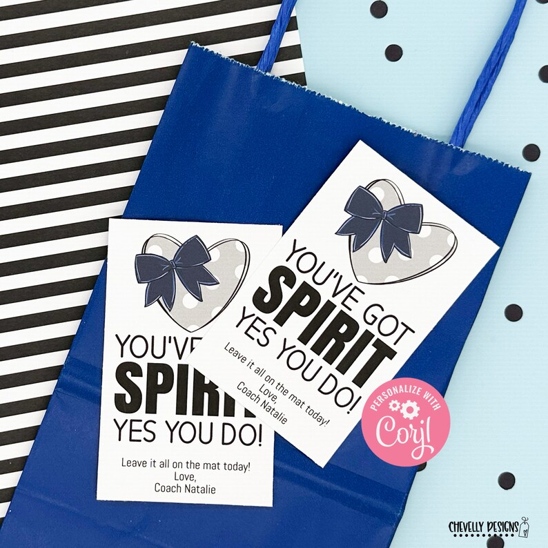 May include: Two white gift tags with a gray heart with white polka dots and a blue bow. The text on the tags reads "You've Got Spirit Yes You Do! Leave it all on the mat today! Love, Coach Natalie".