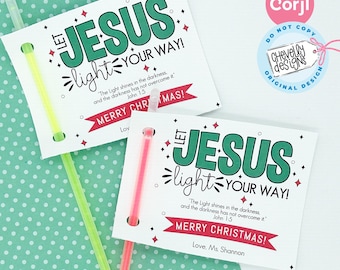 May include: Two white cards with a green and white design. The cards have the text "Let Jesus light your way!" and a Bible verse. The cards are attached to glow sticks. The cards are on a green background with white polka dots.