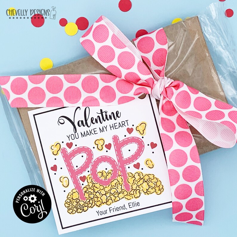 May include: A white gift tag with a pink and white polka dot ribbon tied around it. The tag says "Valentine You Make My Heart Pop" with a picture of popcorn and hearts. The tag is personalized with the name "Ellie".