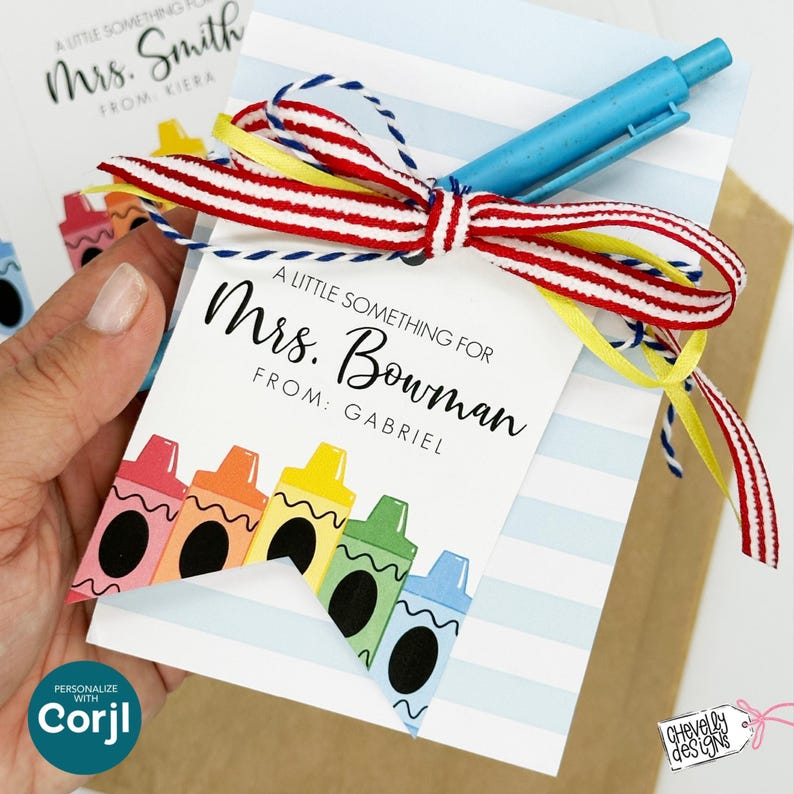 May include: A gift tag with the text "A Little Something For Mrs. Bowman From: Gabriel" and crayon illustrations. The tag is tied with a red, white, and blue ribbon and a blue pen. The tag is held in a person's hand.