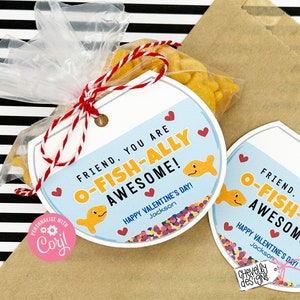 May include: A printable Valentine's Day gift tag with a fishbowl design. The tag says "Friend, you are O-fish-ally awesome!" with a goldfish inside the bowl. The tag is printed on white cardstock and has a red and white twine attached.