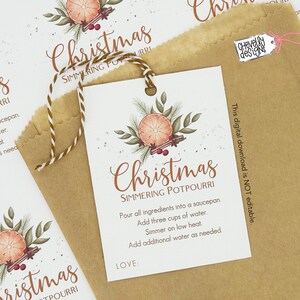 May include: A white tag with the word "Christmas" and "Simmering Potpourri" in brown script, featuring a watercolor orange slice, cinnamon sticks, and greenery. The tag is attached to a brown paper bag with twine.