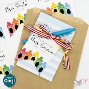 May include: A brown paper gift bag with a blue and white striped card, a blue pen, and a tag that reads "A Little Something For Mrs. Bowman From Gabriel." The tag features crayon illustrations and is tied with a red, white, and yellow ribbon. Additional tags are visible.