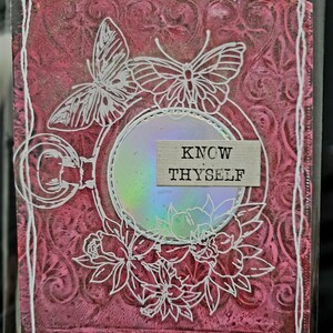 May include: A pink and white mixed media art piece with a butterfly, flowers, and a round iridescent mirror with the text "KNOW THYSELF" in black.