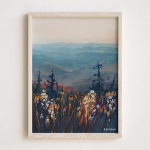 Op de afbeelding: Een ingelijst schilderij van een berglandschap in blauwe en groene tinten. Het schilderij toont een veld met witte bloemen op de voorgrond en een bergketen in de verte op de achtergrond.