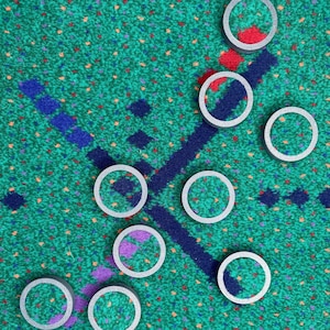 May include: Nine round, gray, decorative coasters with different patterns on a green and blue patterned surface.