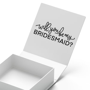 May include: White gift box with a lid that opens to reveal the text "Will you be my bridesmaid?" in black script.