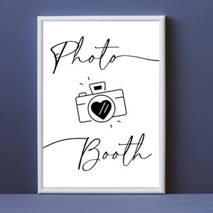 May include: A white sign with black text and a camera icon that says "Photo Booth".