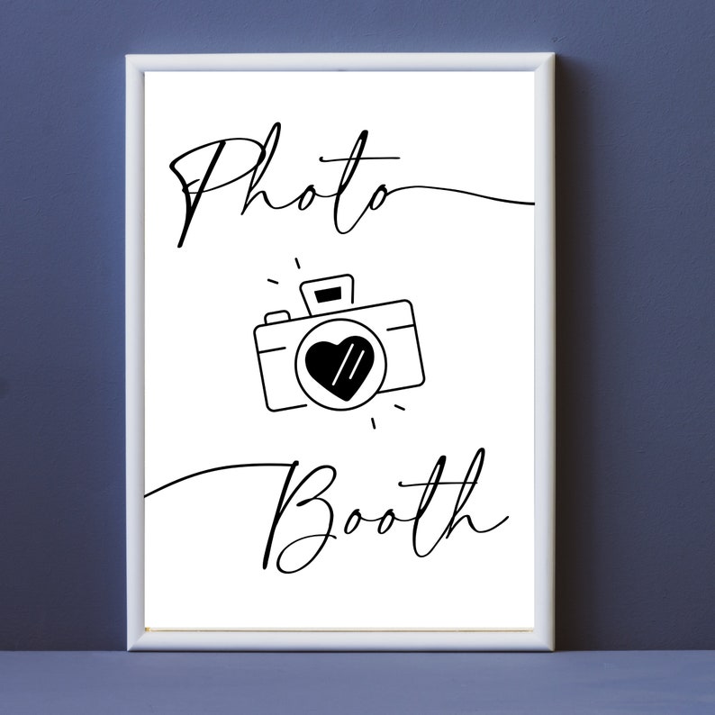 May include: A white sign with black text and a camera icon that says "Photo Booth".