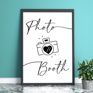 May include: Black and white printable sign with the text "Photo Booth" and a simple line drawing of a camera with a heart in the lens.