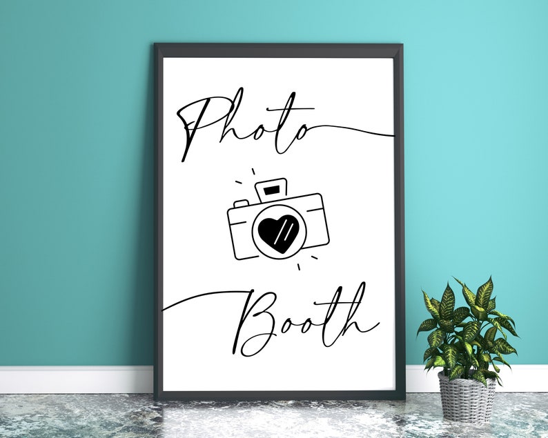 May include: Black and white printable sign with the text "Photo Booth" and a simple line drawing of a camera with a heart in the lens.