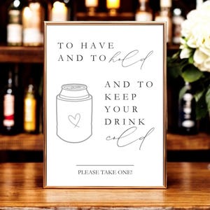 May include: A rectangular sign in a thin gold frame with white background and black text that reads: TO HAVE AND TO hold AND TO KEEP YOUR DRINK cold. Below the text is a line drawing of a beverage can cooler with a small heart and the text PLEASE TAKE ONE!