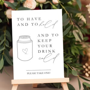 May include: A white rectangular sign with black text that reads TO HAVE AND TO hold AND TO KEEP YOUR DRINK cold and PLEASE TAKE ONE! The sign features a line drawing of a beverage can cooler with a small heart outline on the front surface.