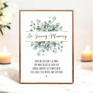 May include: A framed print with the words "In Loving Memory" in elegant script, above a watercolor eucalyptus design. The print includes a heartfelt poem and is surrounded by a gold frame. Candles and flowers are in the background.